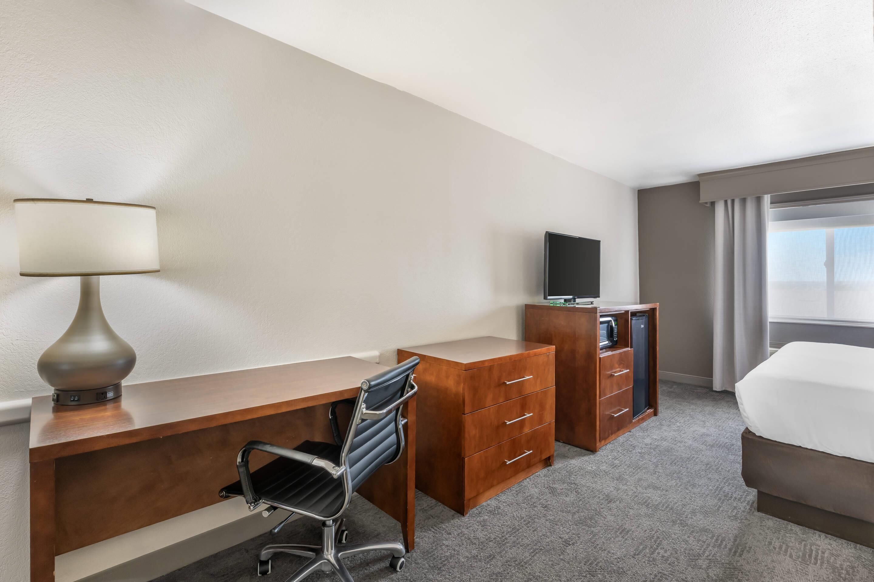 A hotel room with a desk, chair, TV, wardrobe, and bed.
