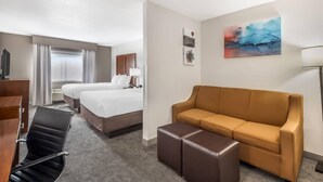 Una habitación de hotel con cama, sofá, sillón, escritorio y un cuadro en la pared.