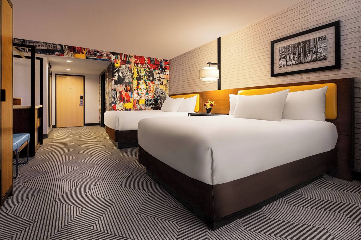 Ein Hotelzimmer mit zwei Betten, einem gemusterten Teppich, einer Ziegelwand und einem gerahmten Bild.