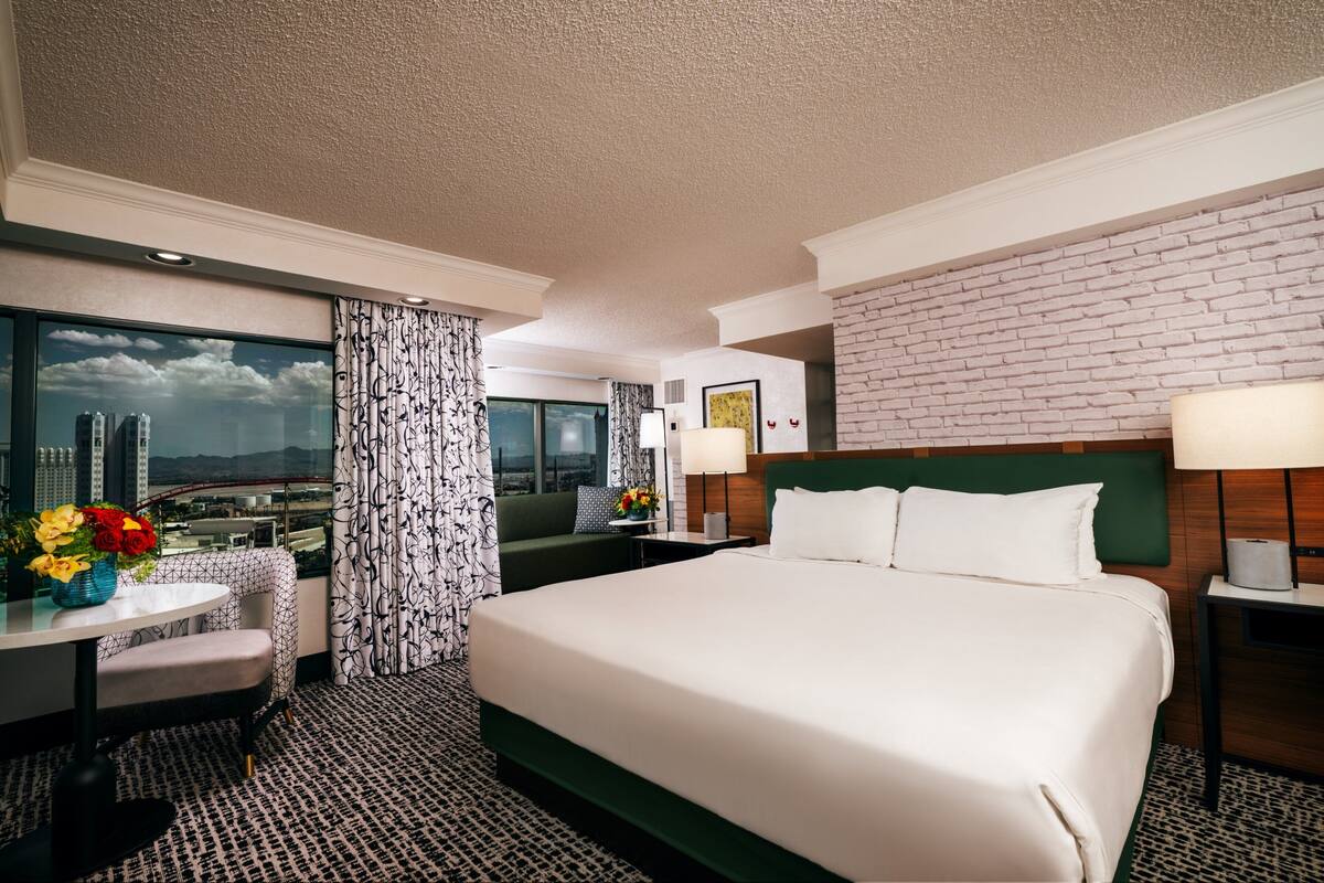 Ein Hotelzimmer mit einem großen Bett, einem Schreibtisch mit Stuhl, Blick auf die Stadtlandschaft und einer Wand mit Ziegeln.