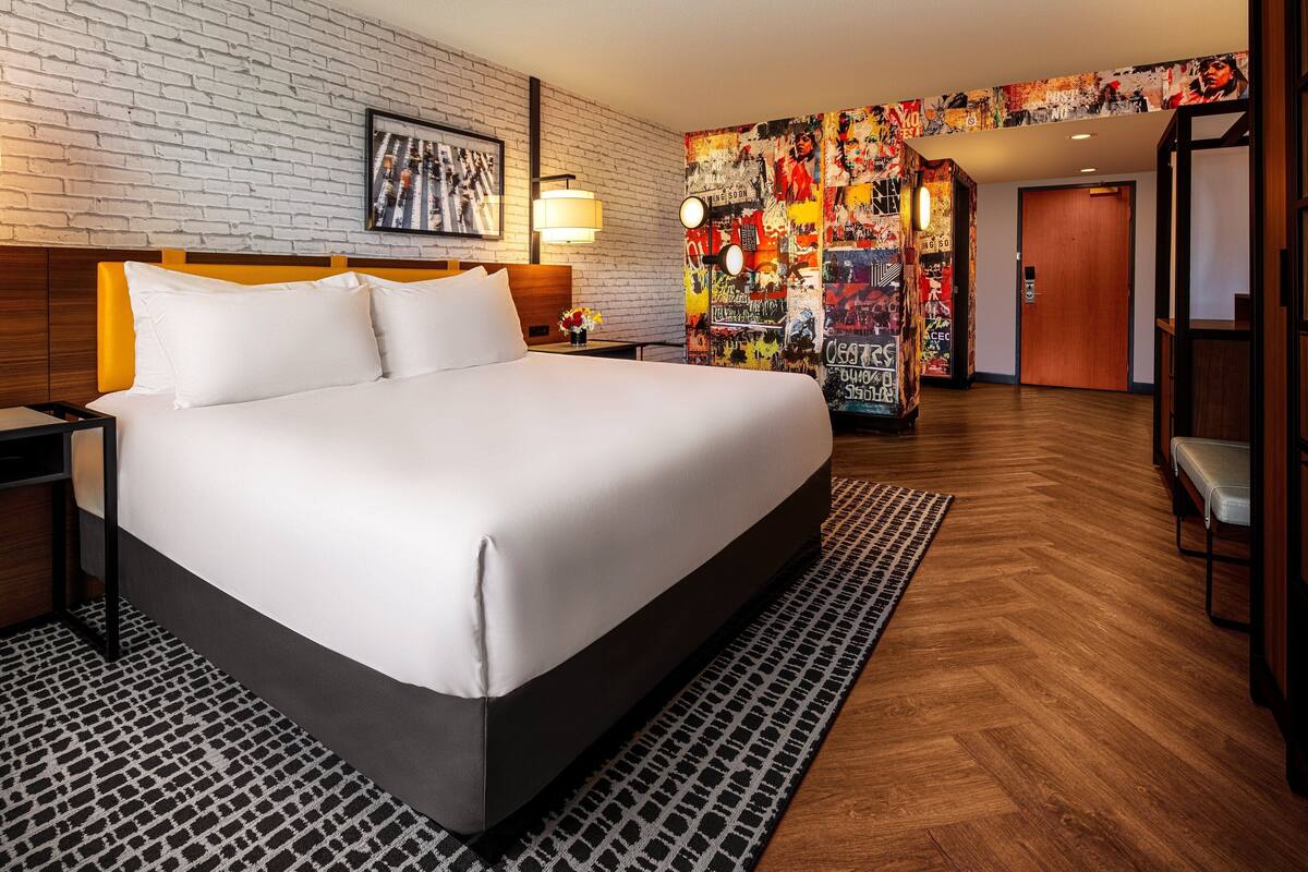 Ein Hotelzimmer mit einem großen Bett, einer Backsteinwand, einem farbenfrohen Wandgemälde und Holzboden.