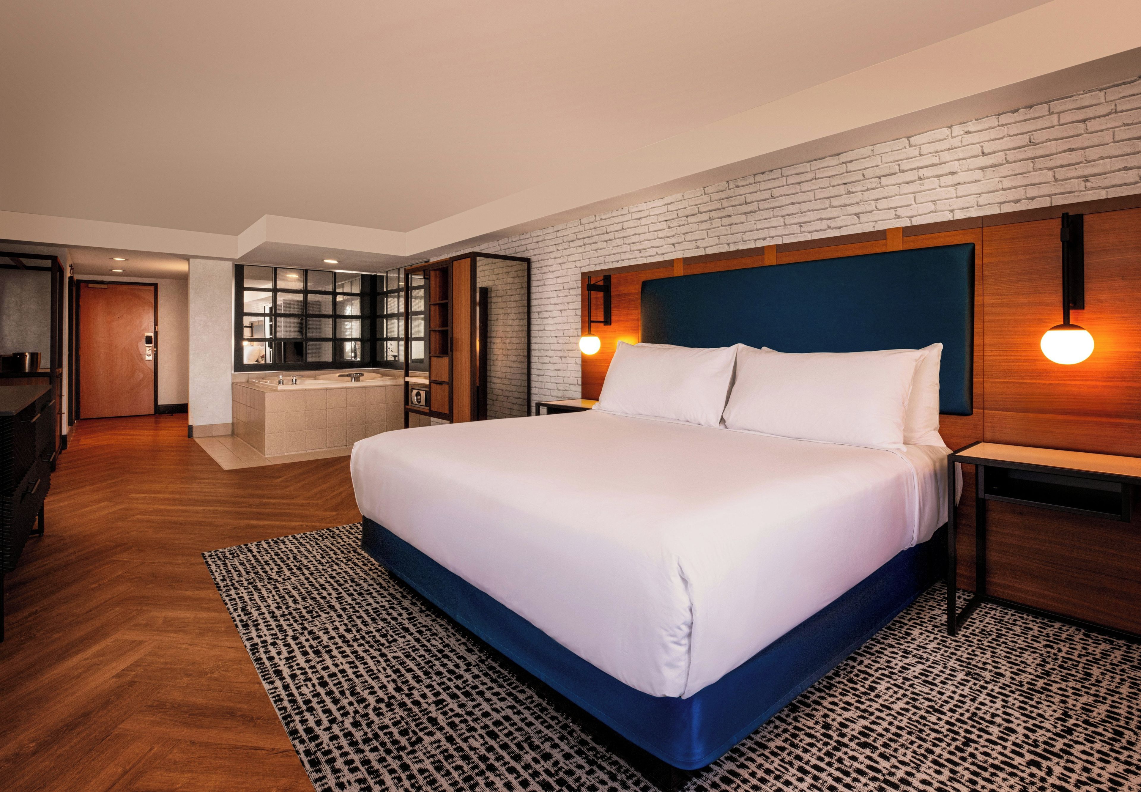 Una habitación de hotel moderna con una cama grande, un escritorio integrado, una zona de estar y un baño con bañera.