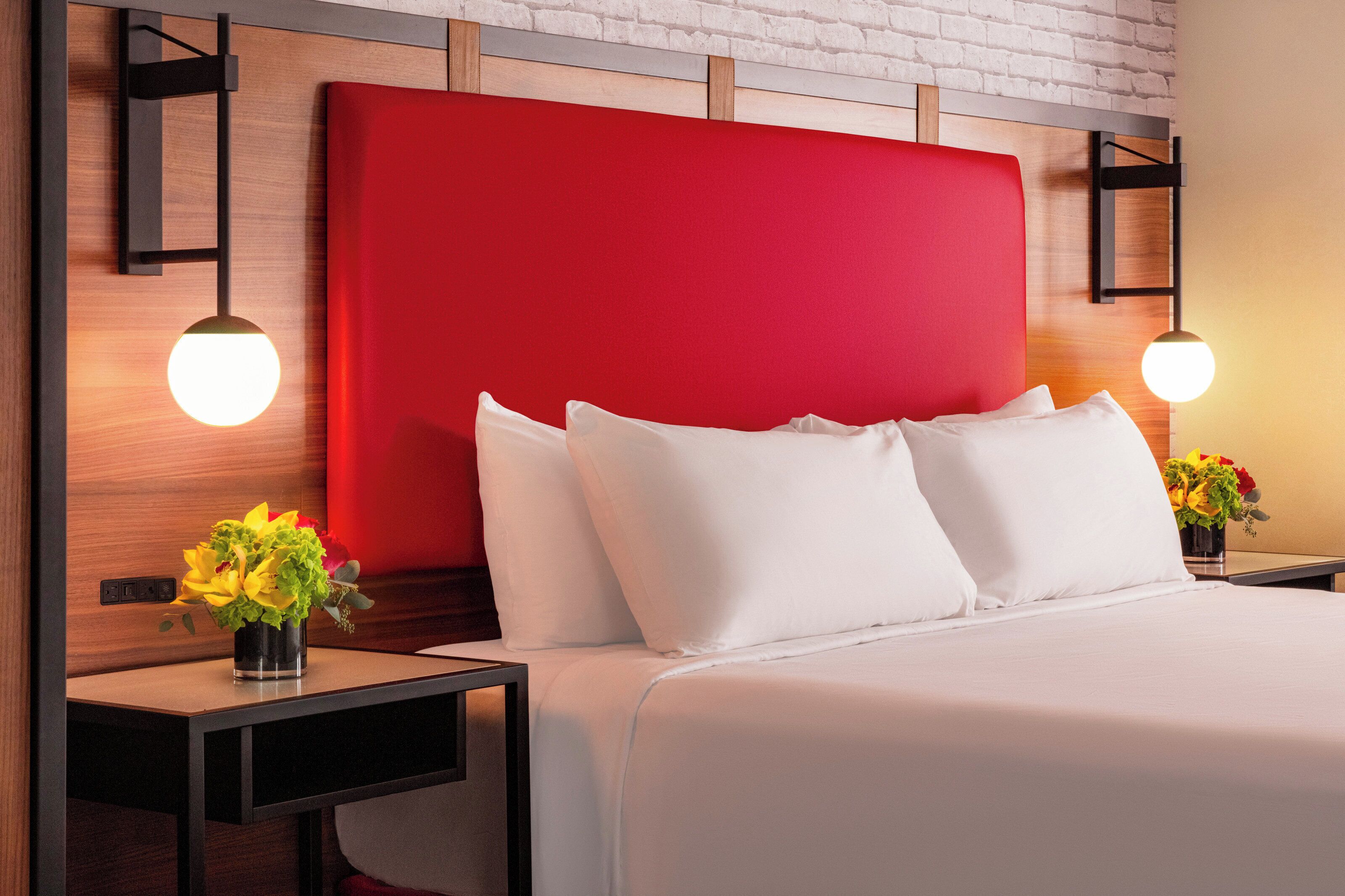 A hotel room with a red headboard, white bedding, and two bedside tables with lamps and flower vases.