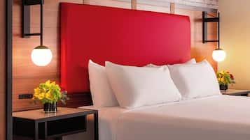 A hotel room with a red headboard, white bedding, and two bedside tables with lamps and flower vases.