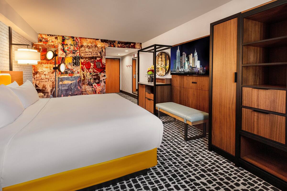 Ein Hotelzimmer mit Bett, einer Bank, einer Wand mit Stadtblick-Poster und einem gemusterten Boden.