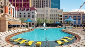 A large outdoor swimming pool with lounge chairs and umbrellas, surrounded by buildings. - New York-New York Hotel & Casino (Las Vegas)