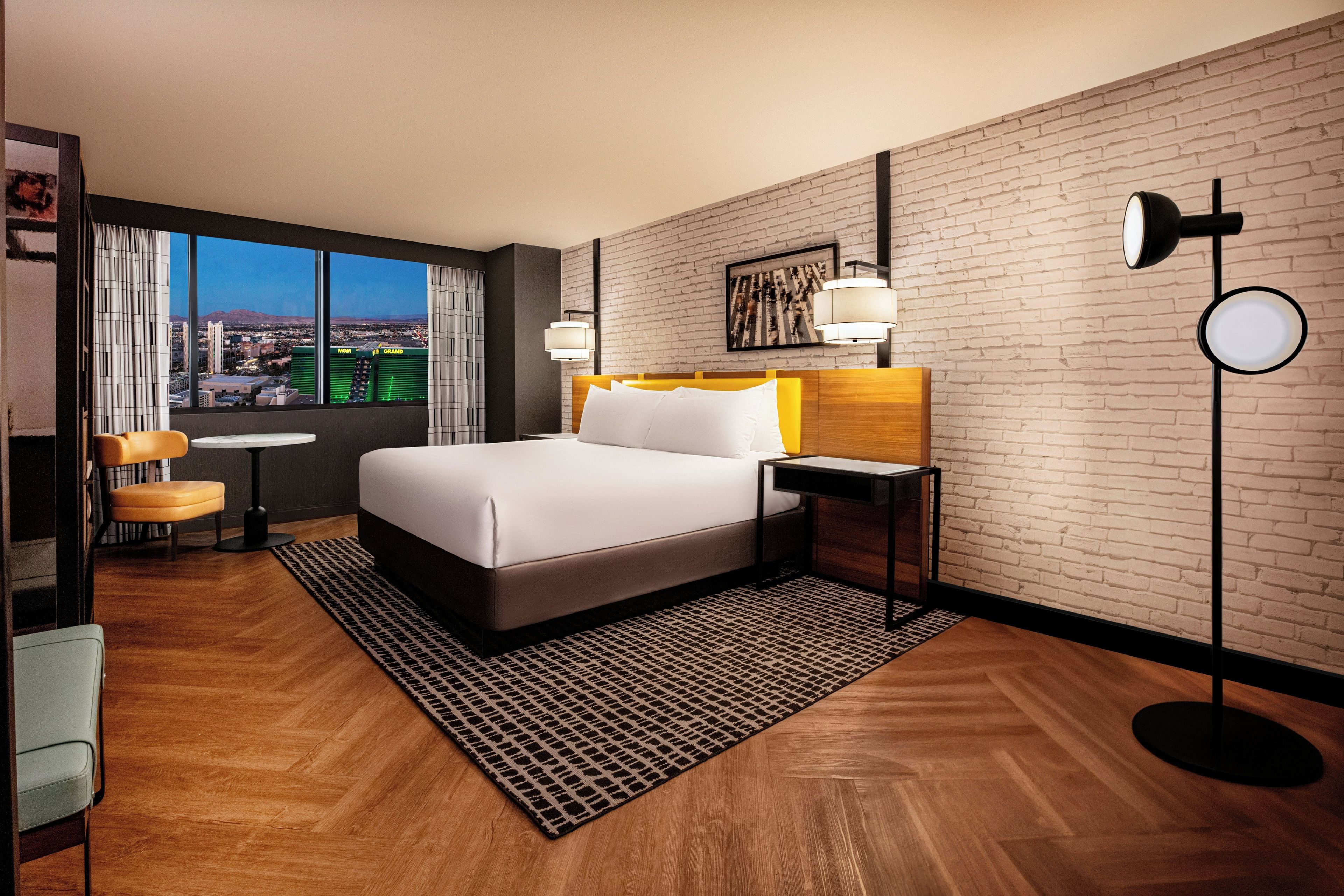 Une chambre d’hôtel avec un grand lit, un bureau, une chaise et une vue sur le paysage urbain par la fenêtre.