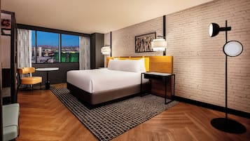 Une chambre d’hôtel avec un grand lit, un bureau, une chaise et une vue sur le paysage urbain par la fenêtre.
