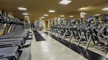 A gym with multiple treadmills and exercise machines, a black and white floor, and a mirrored wall.