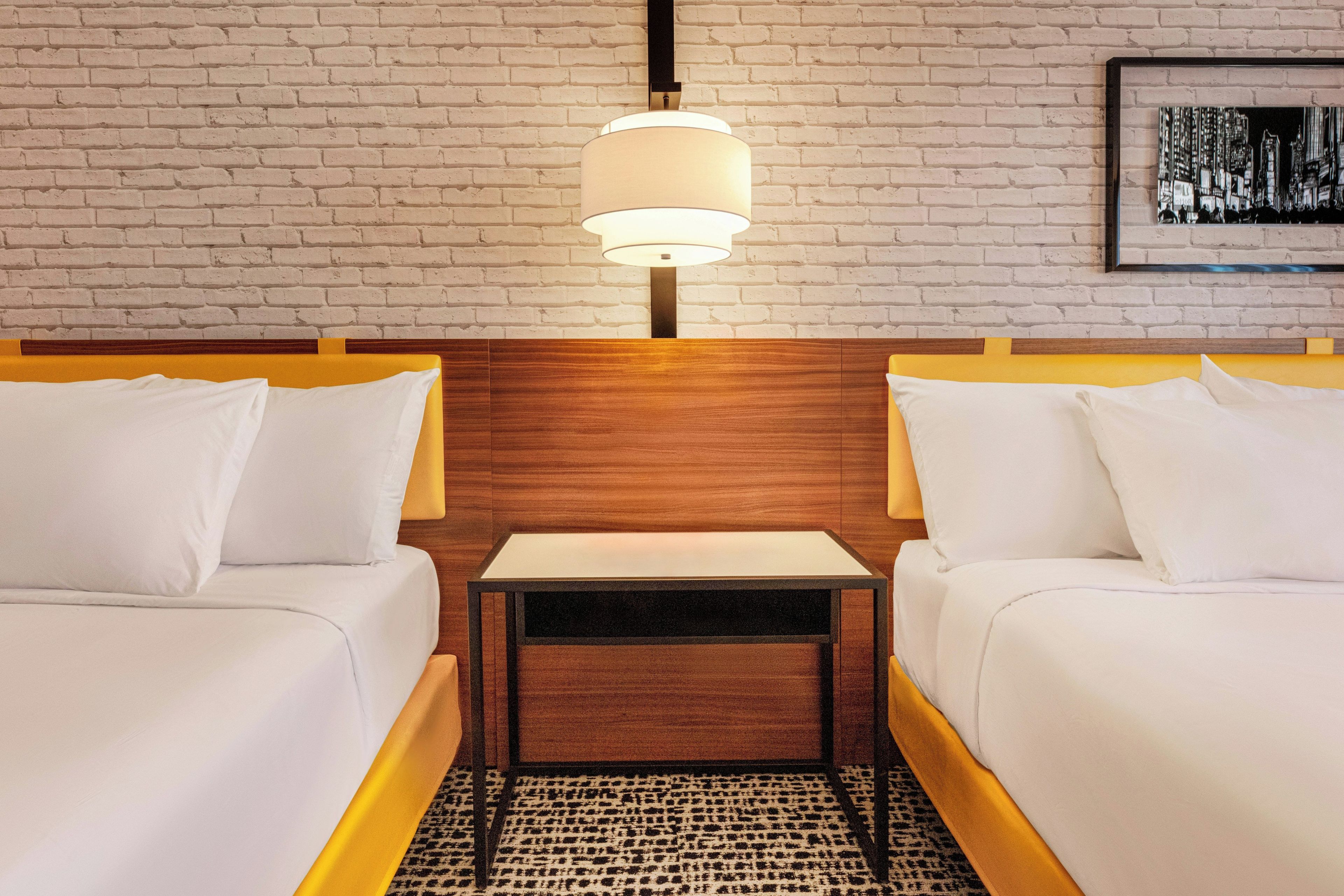 Une chambre d’hôtel avec deux lits, une table de chevet, une lampe et un mur en briques.