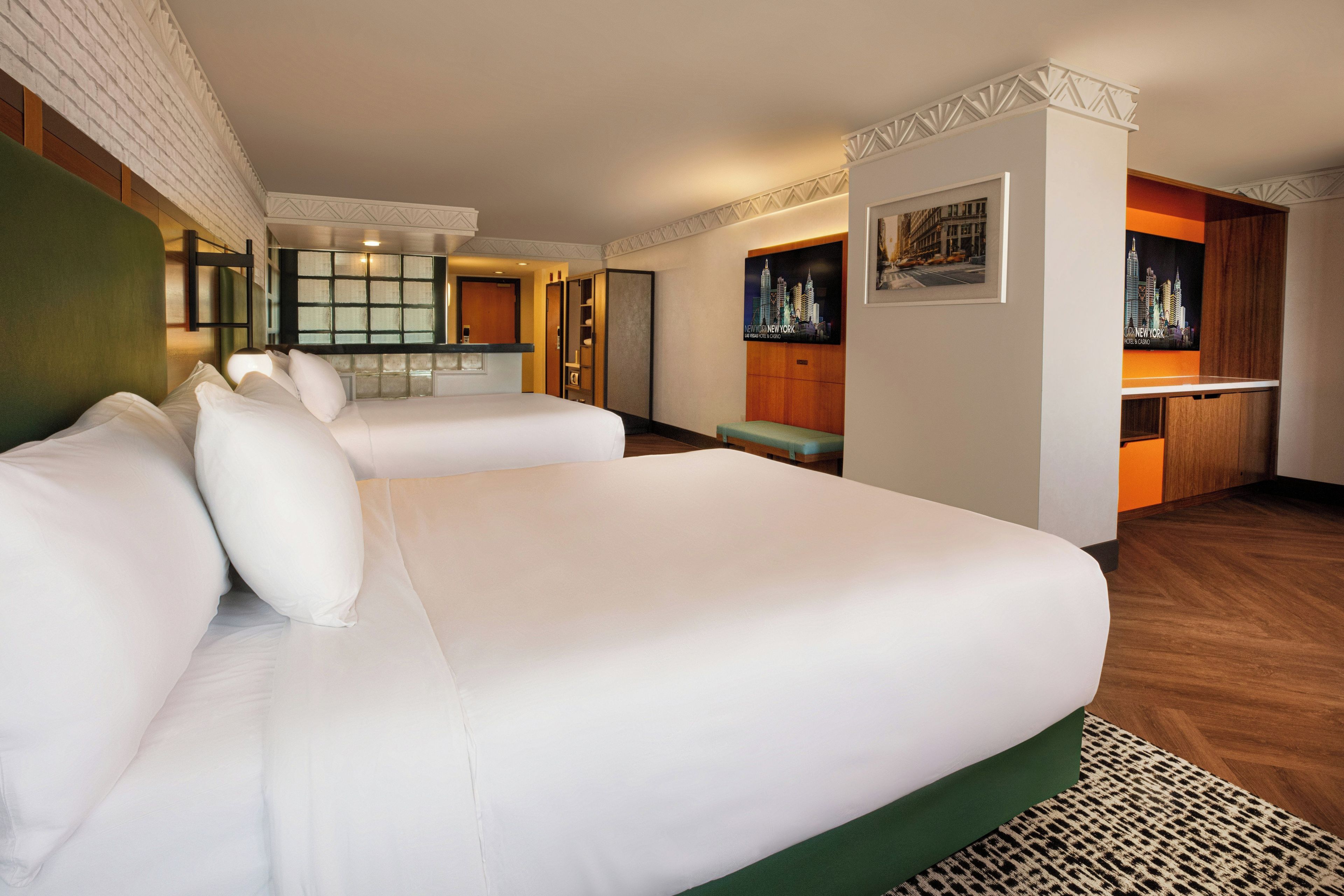 A hotel room with two beds, a small kitchenette, and a cityscape poster on the wall.