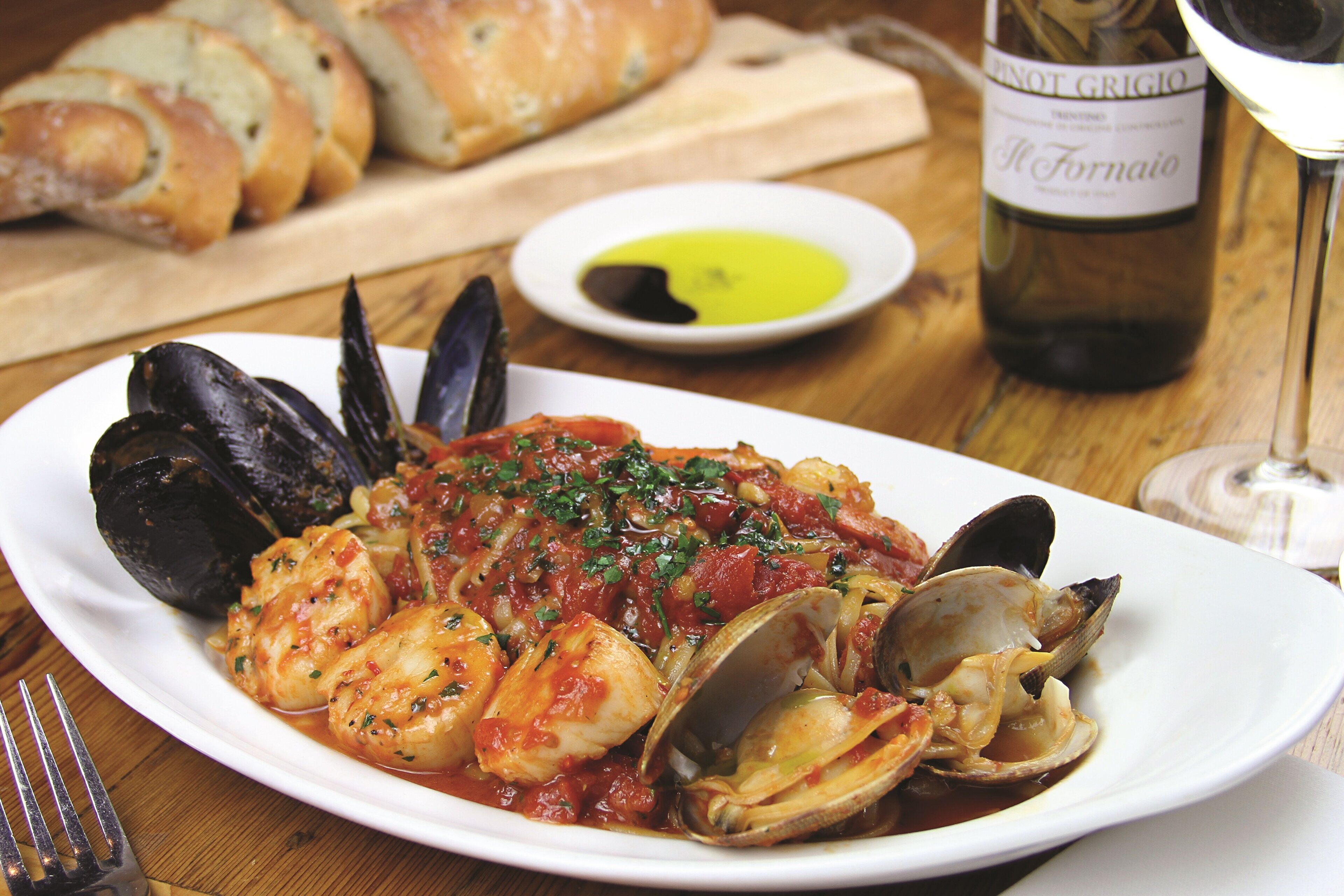 A plate of seafood pasta with mussels and clams, a bottle of wine, and a glass of wine on a wooden table.