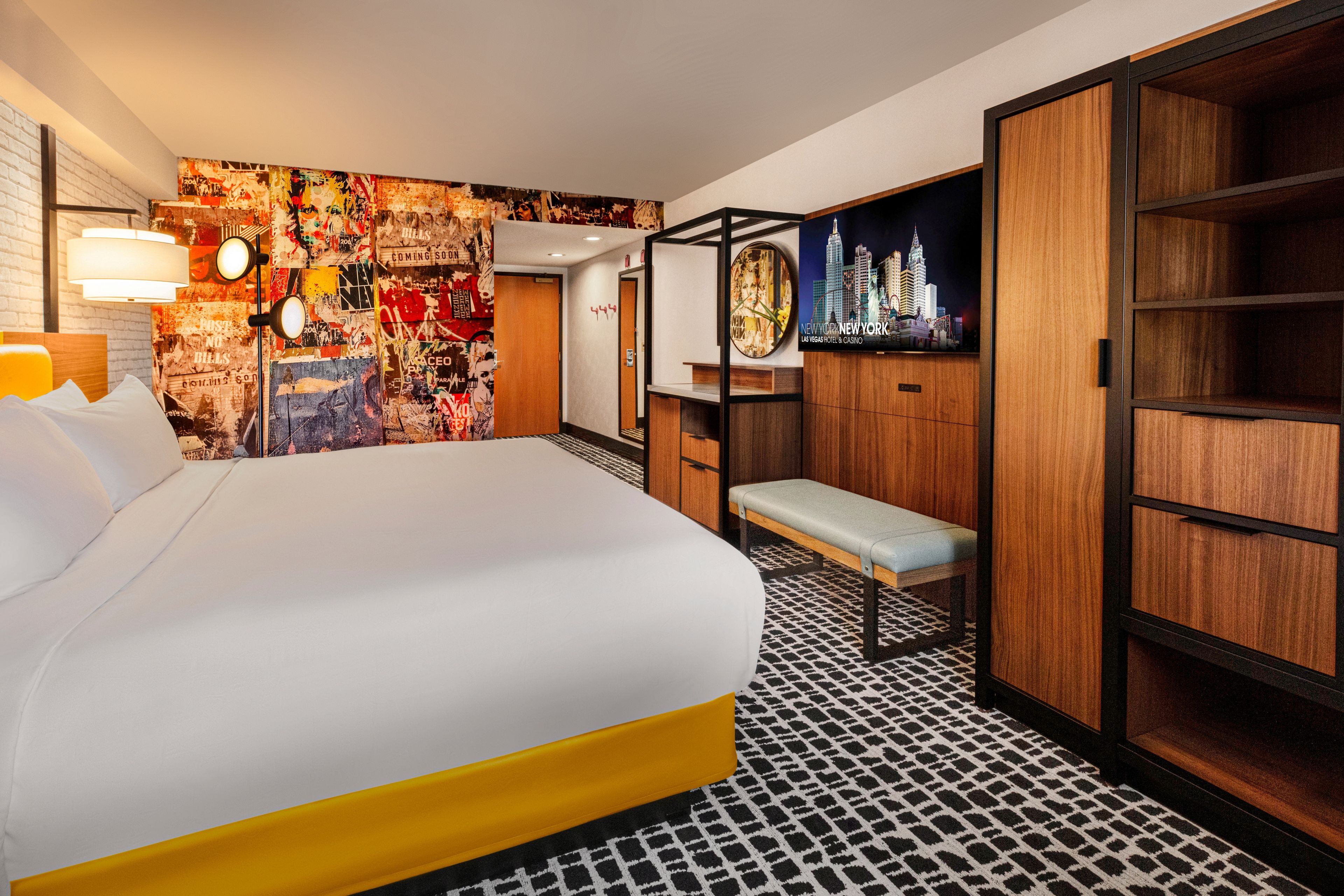 A hotel room with a bed, a bench, a wardrobe, and a wall with a cityscape poster.