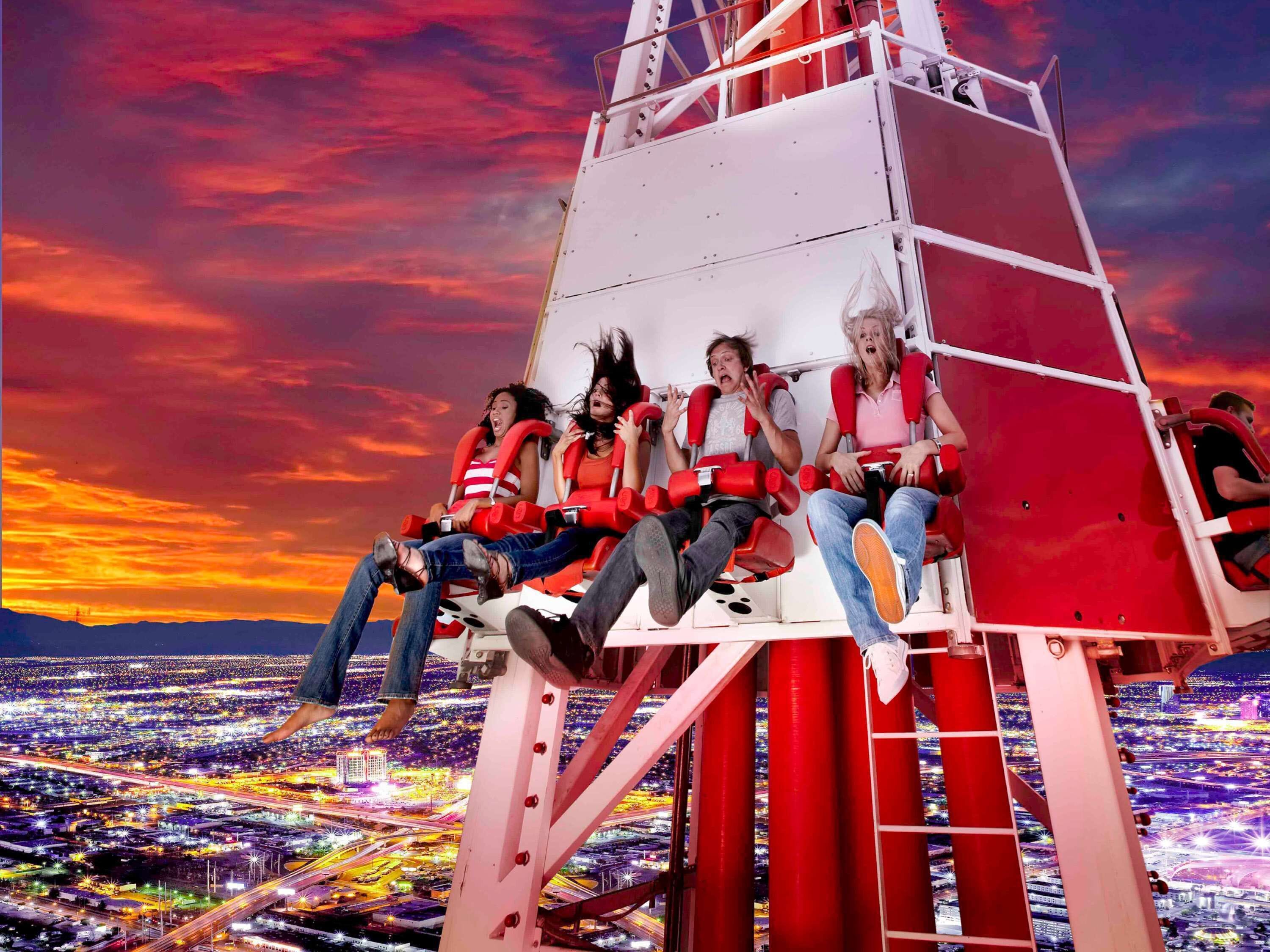 Um grupo de pessoas em uma atração de parque de diversões, com um horizonte urbano ao fundo.