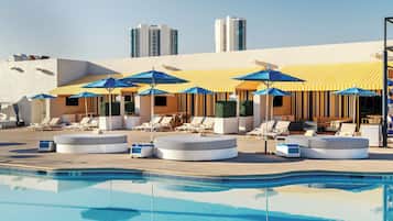 A poolside area with lounge chairs and umbrellas, a pool, and high-rise buildings in the background.