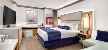 A hotel room with a television, a dining table, a sofa, a chair, a coffee table, and a bed. at The STRAT Hotel, Casino & Tower
