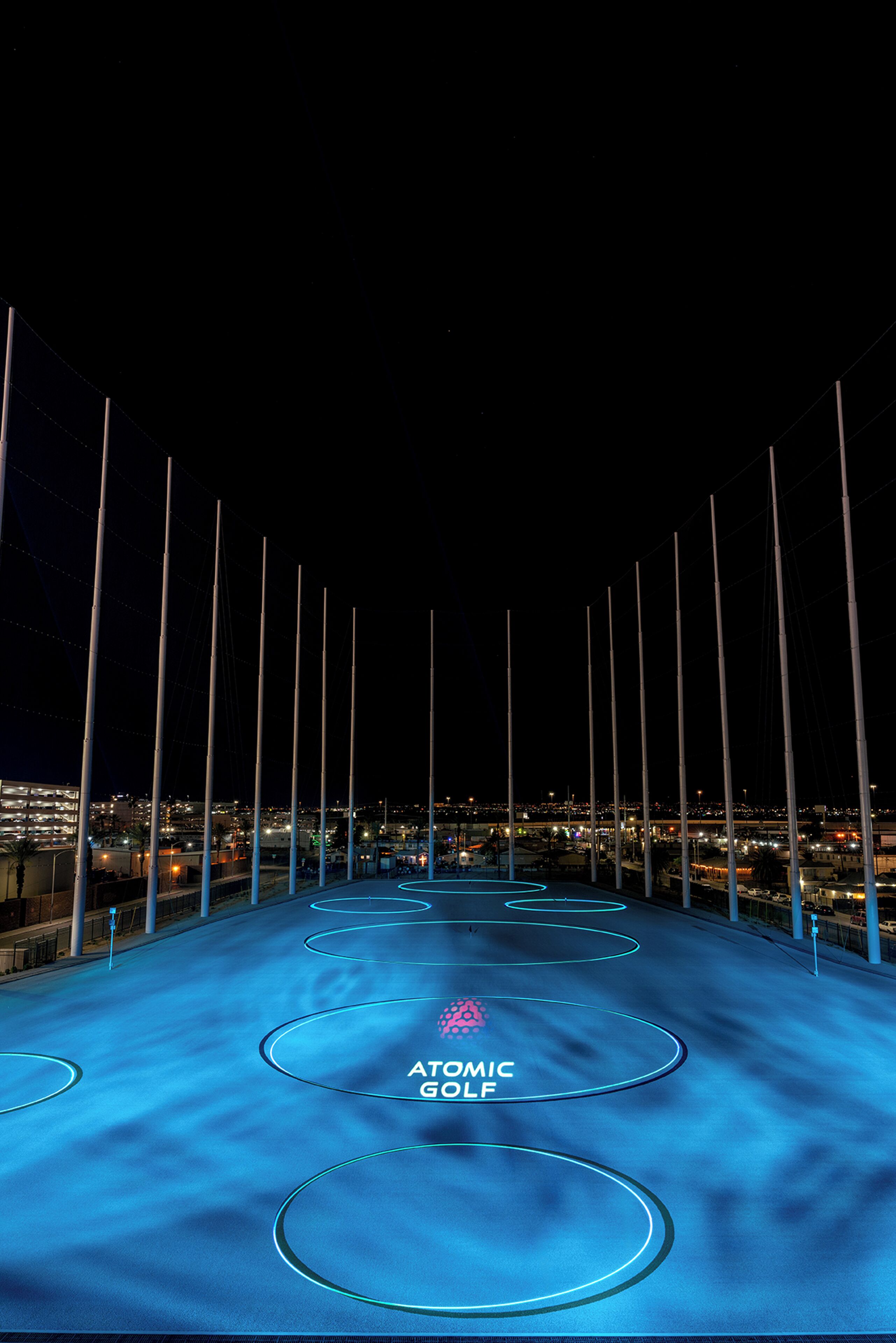 Vista nocturna de una azotea con diseños circulares iluminados y el texto "ATOMIC GOLF".