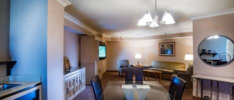 Habitación de hotel con una mesa de comedor, sillas, un sofá, un televisor, una lámpara y un espejo.
