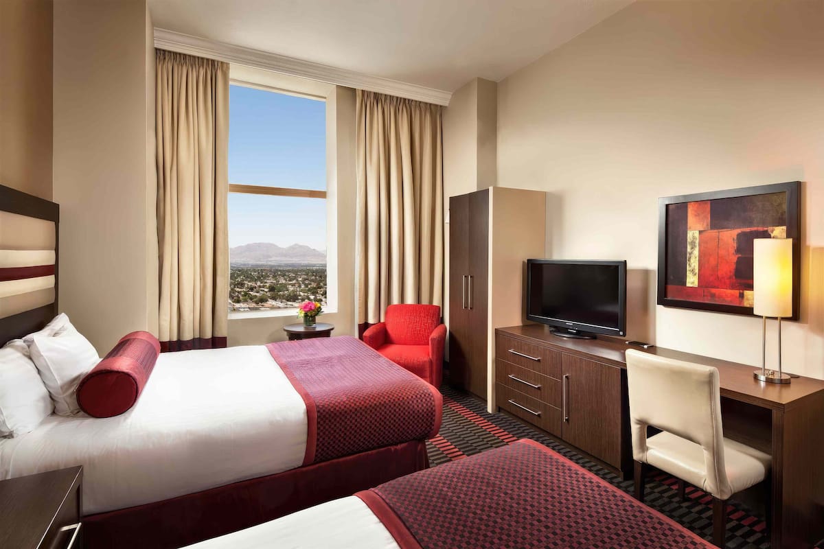 Habitación de hotel con dos camas, un escritorio, televisión y vistas a las montañas.