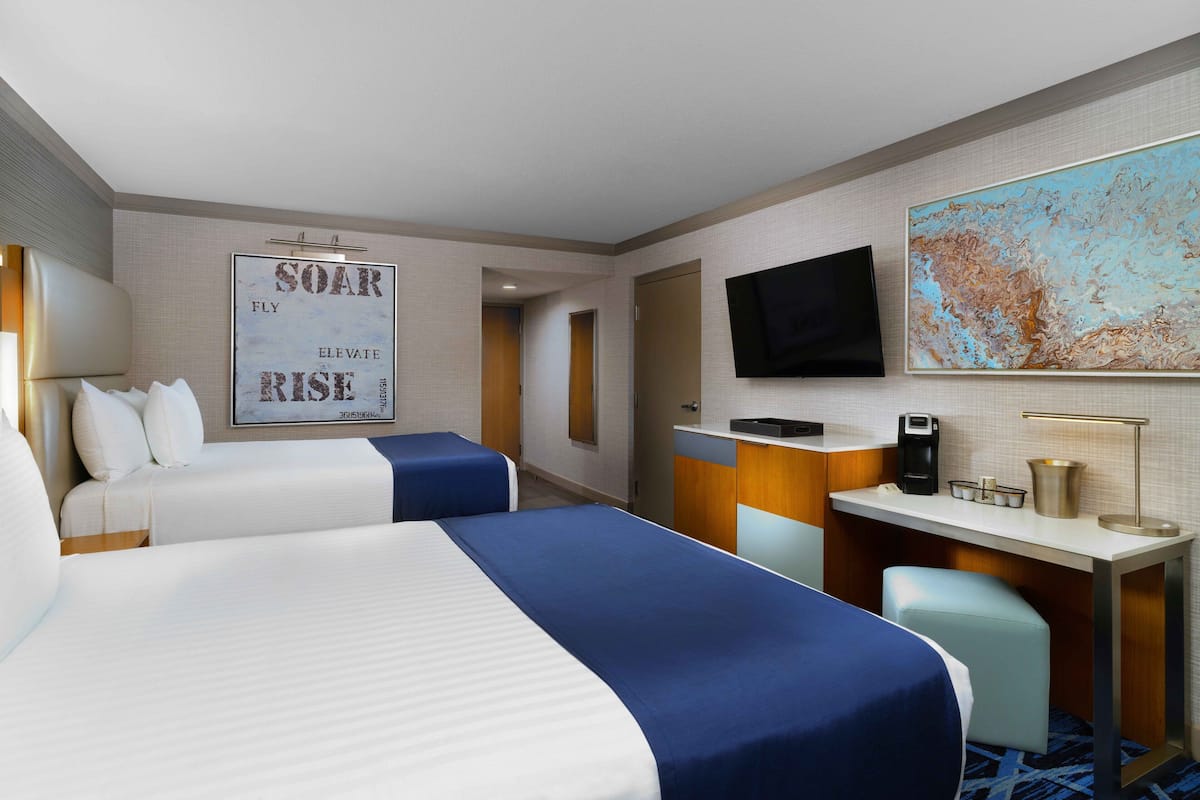 Una habitación de hotel con dos camas, un escritorio, un televisor y un cartel motivacional.