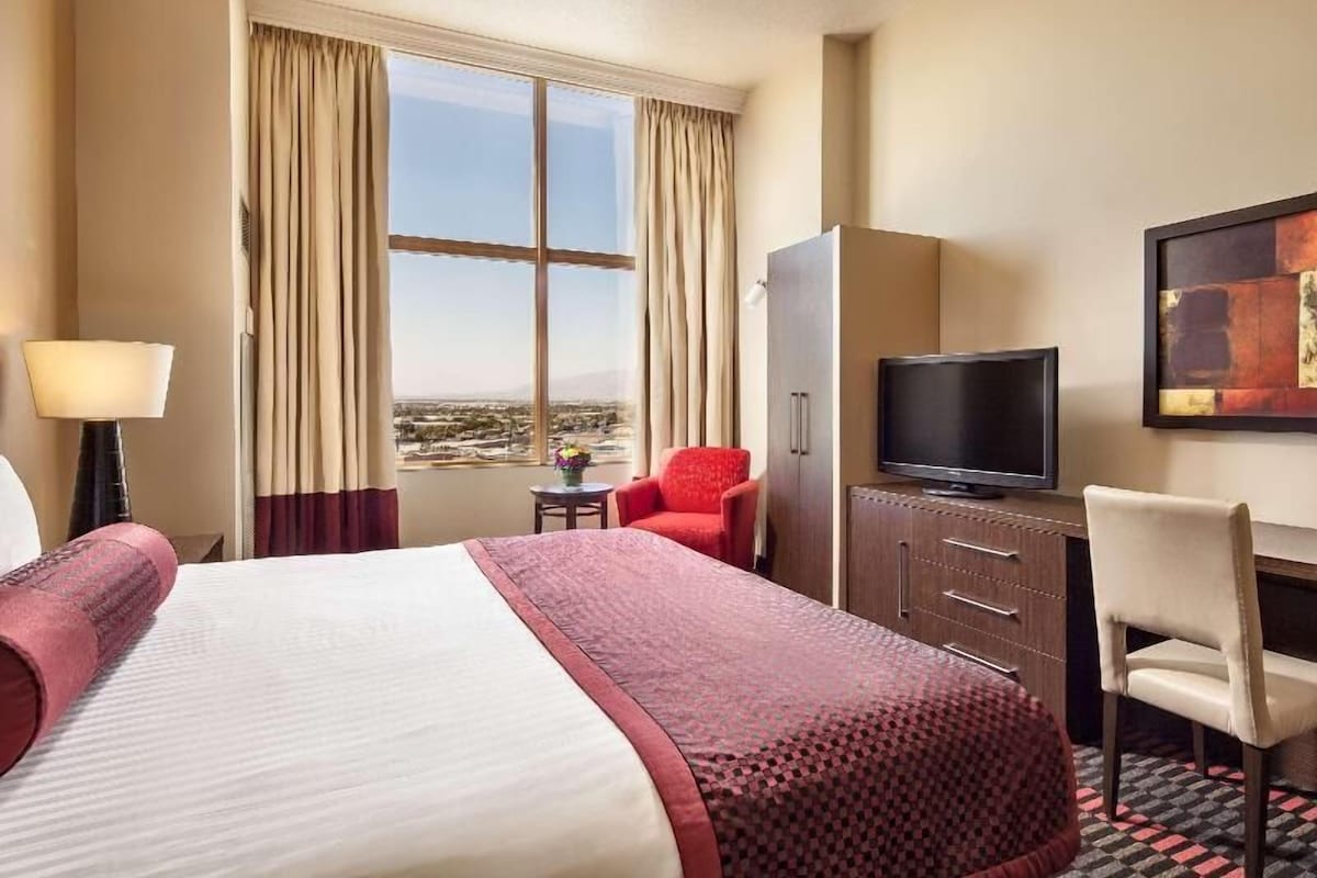 A hotel room with a bed, a television, a desk, a chair, a lamp, and a window with curtains.