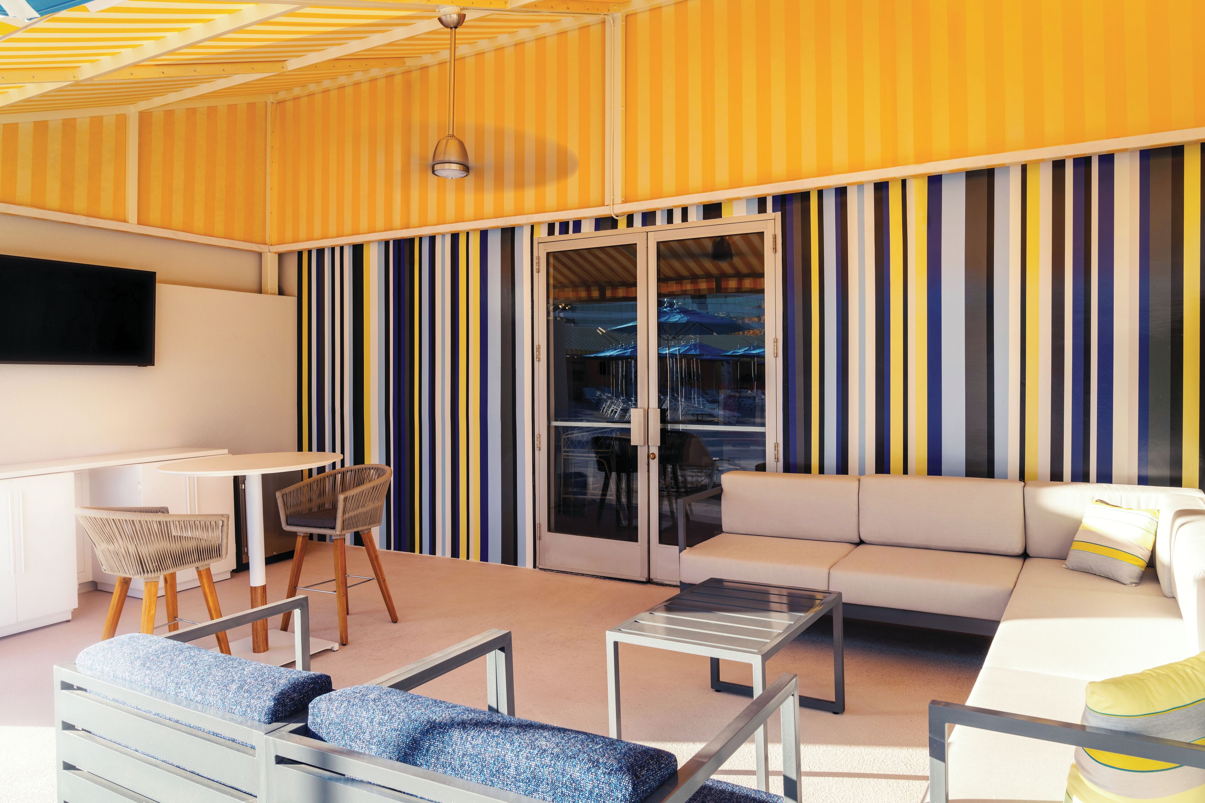 A modern outdoor living area with a sofa, chairs, a table, and a TV mounted on the wall.