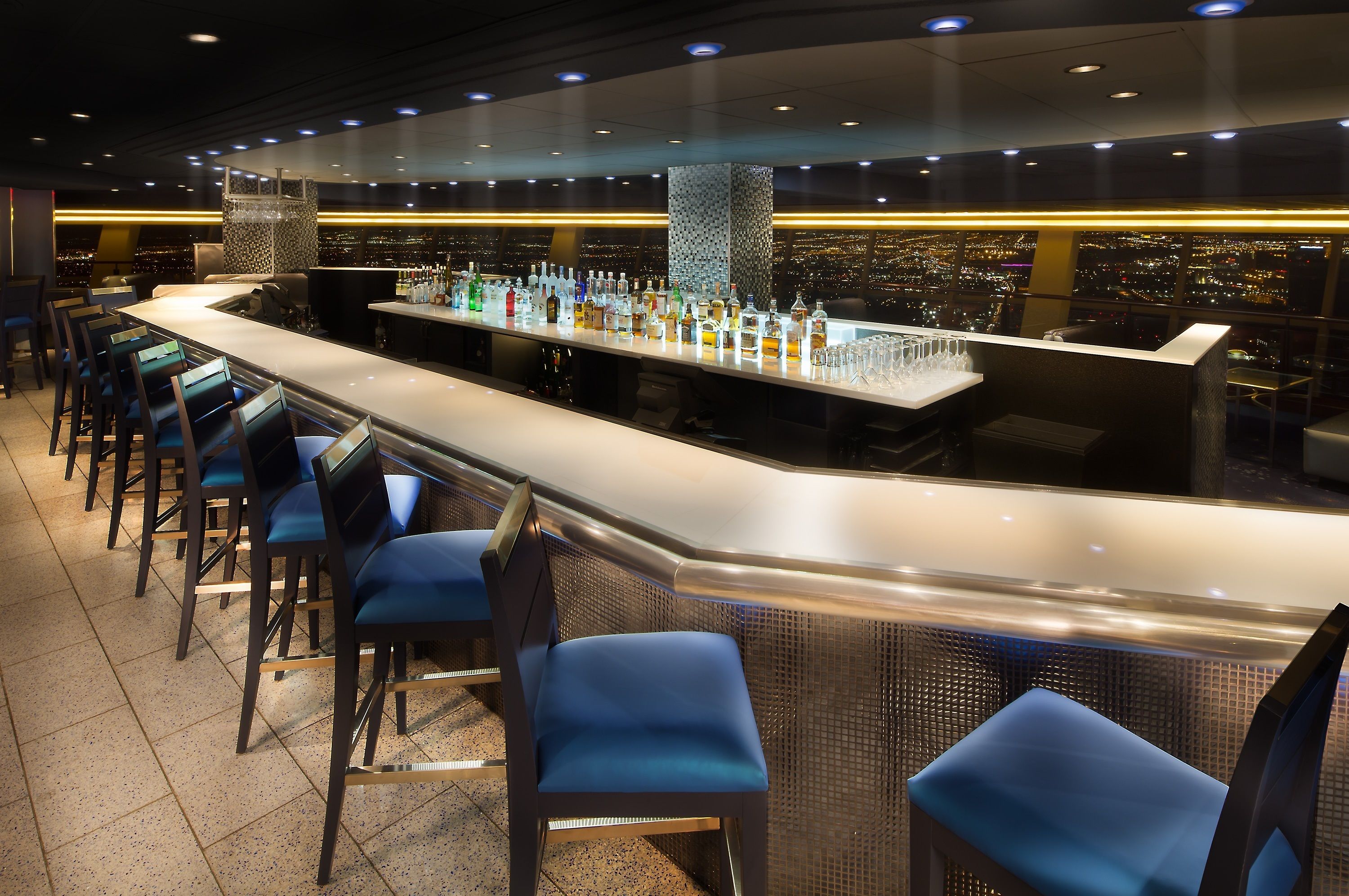 Un bar avec vue sur la ville, des tabourets et un grand choix de bouteilles.