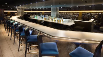 Un bar avec vue sur la ville, des tabourets et un grand choix de bouteilles.