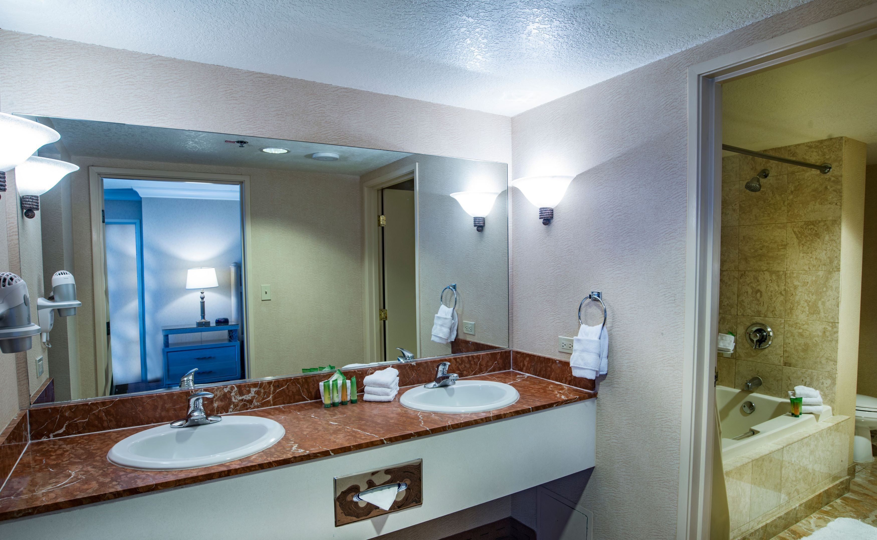 A hotel bathroom with two sinks, a large mirror, a shower, and a towel rack.