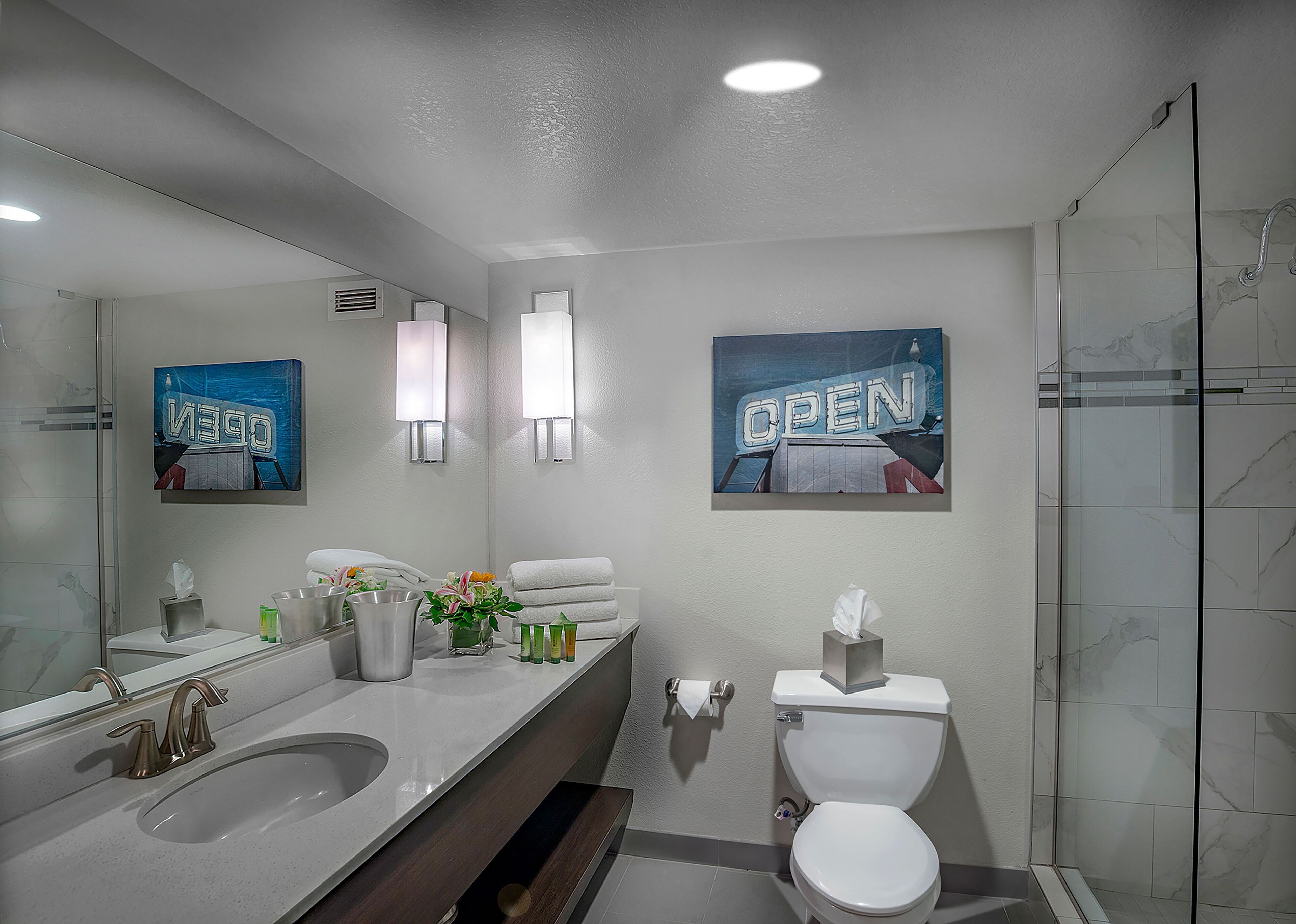 A modern bathroom with a large mirror, two sinks, a toilet, and a shower.