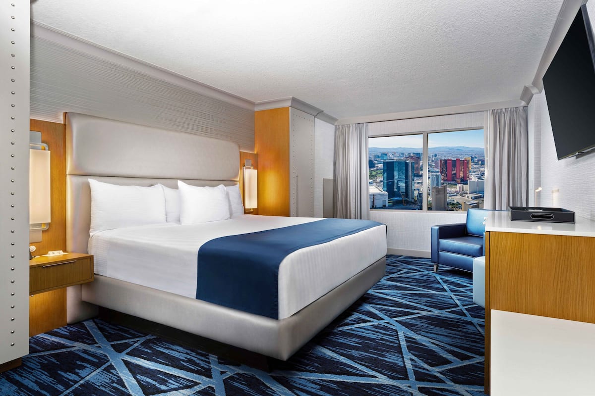 Habitación de hotel con una cama grande, un escritorio, una silla, un televisor y vistas a la ciudad.