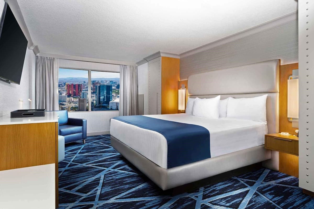 Habitación de hotel con una cama grande, un escritorio, un televisor y vista a la ciudad.
