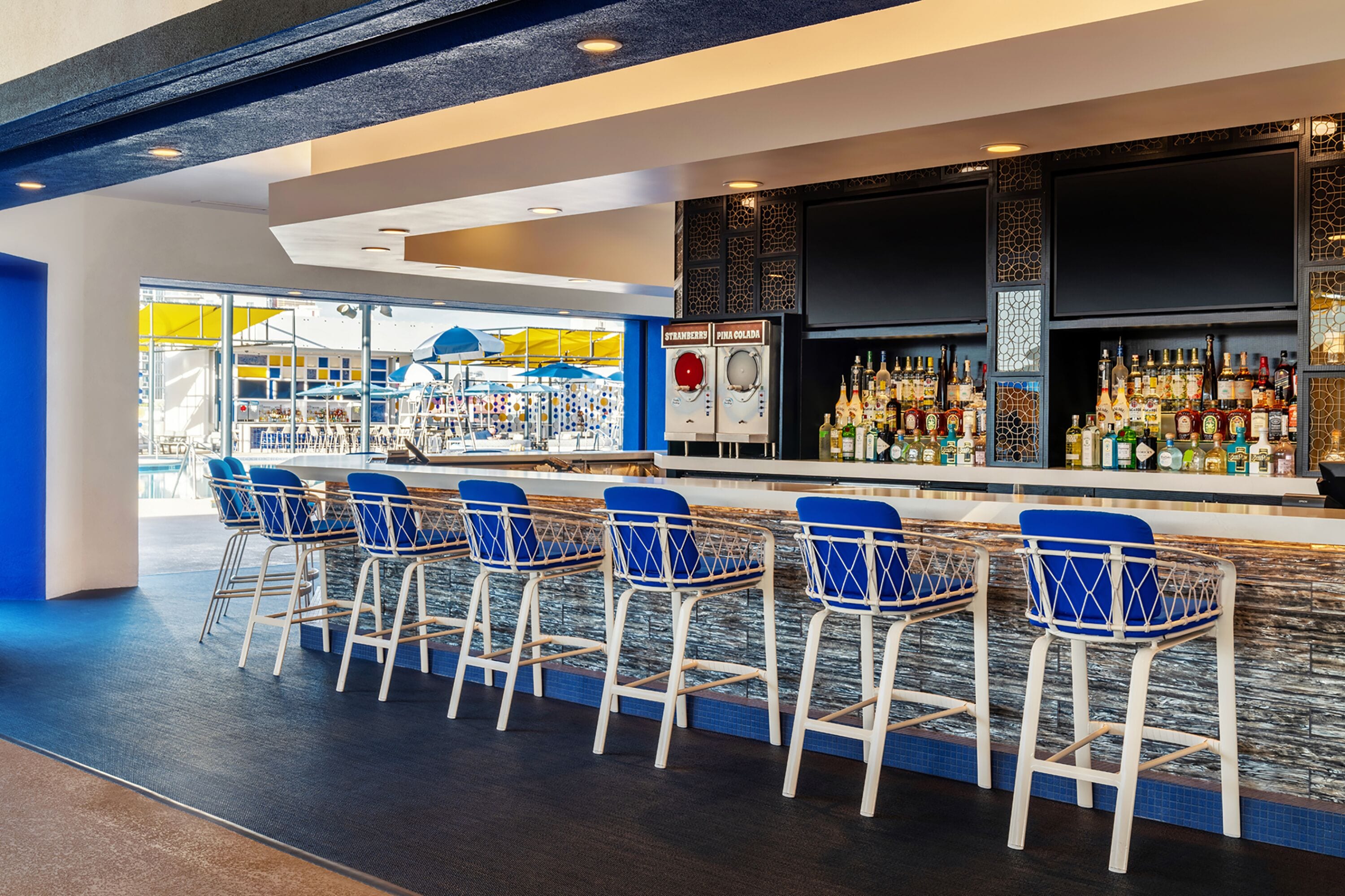 A bar area with a long counter, multiple stools, and a variety of bottles.