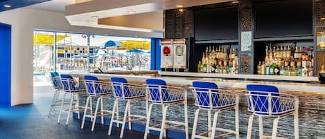 A bar area with a long counter, multiple stools, and a variety of bottles.
