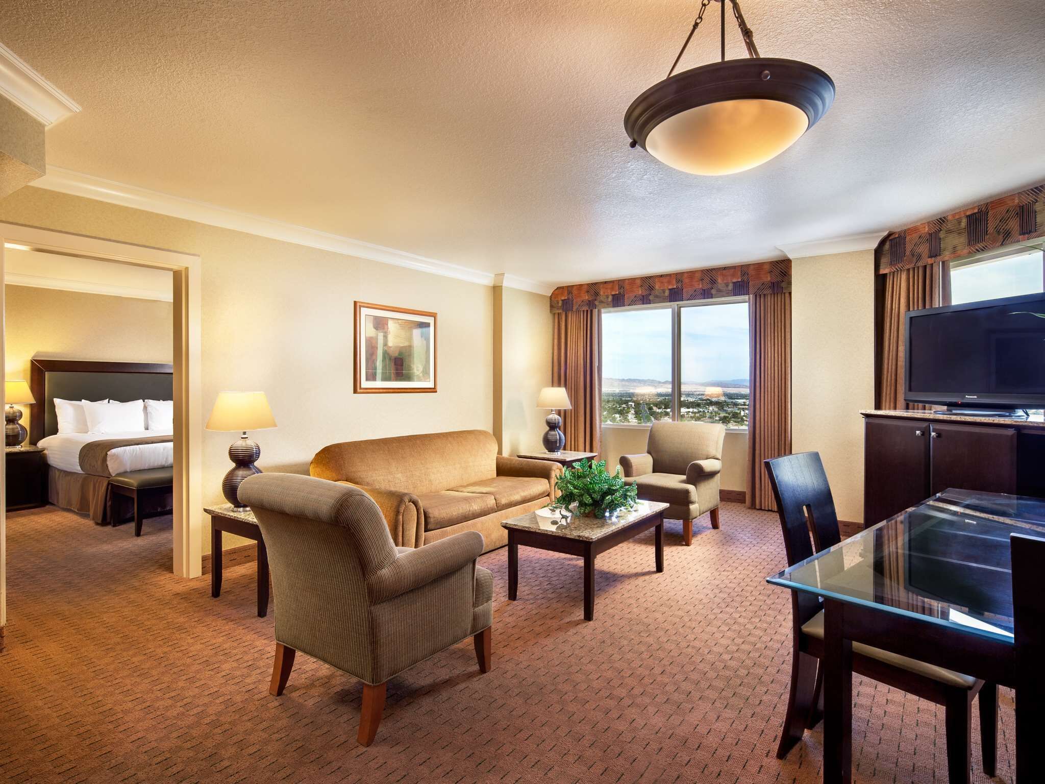 Habitación de hotel con cama, sofá, mesa de centro, televisor y vista a la ciudad.