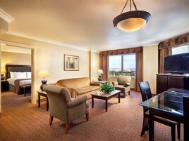 Habitación de hotel con cama, sofá, mesa de centro, televisor y vista a la ciudad.