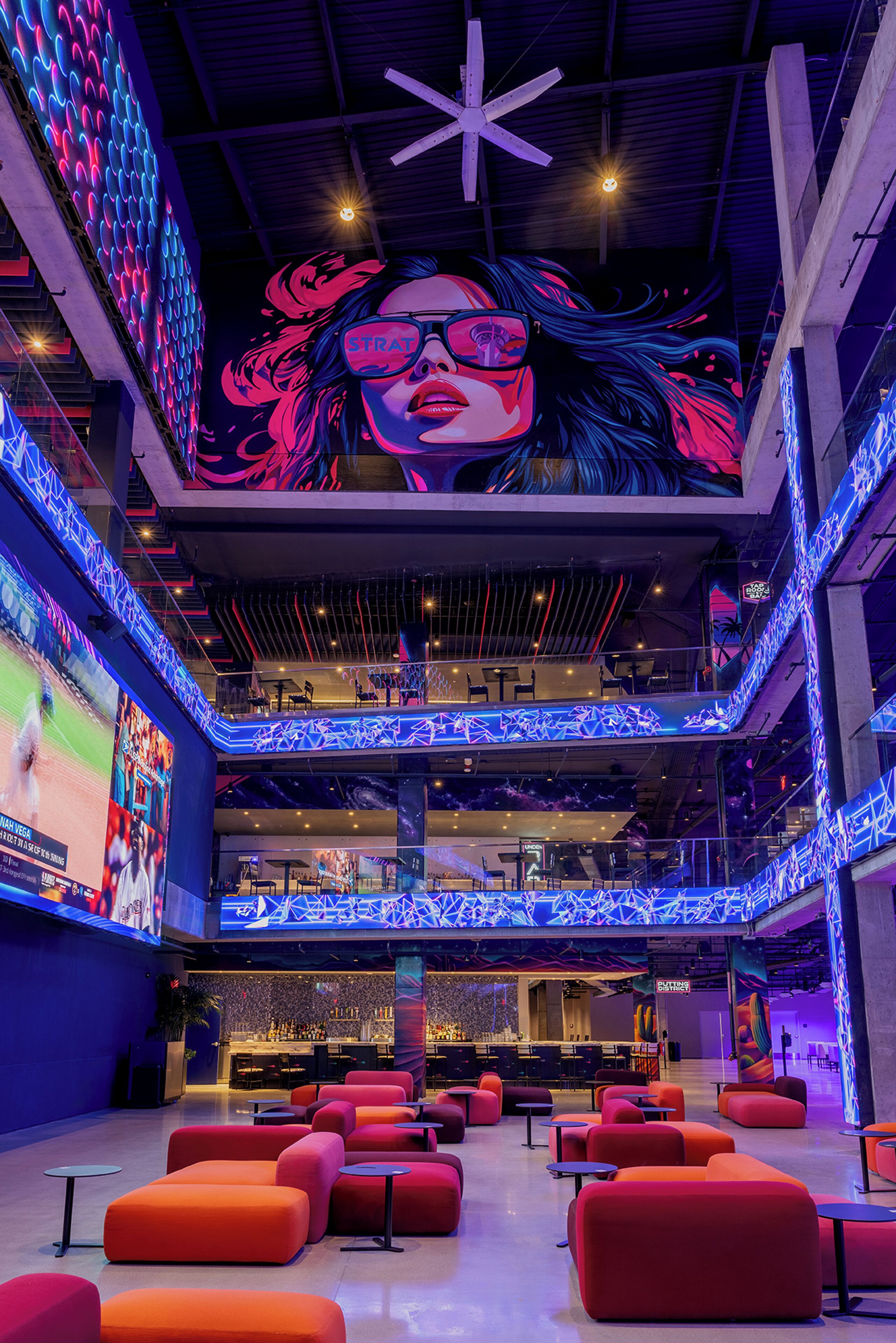 Un espace intérieur à plusieurs niveaux, comprenant des coins salon, un bar et un grand écran numérique affichant une image.