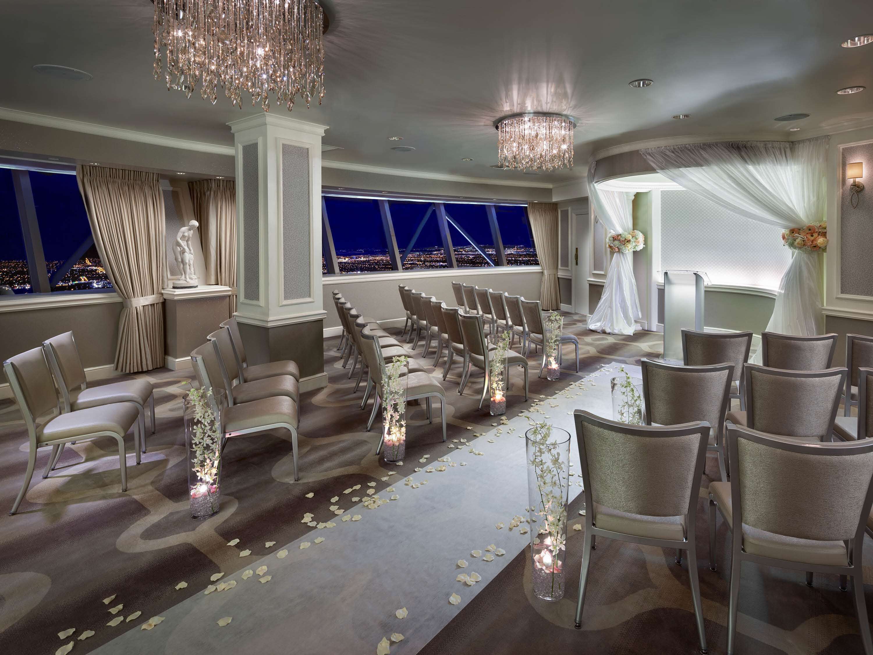 Une cérémonie de mariage avec des rangées de chaises, des décorations florales et une vue sur la ville illuminée la nuit.