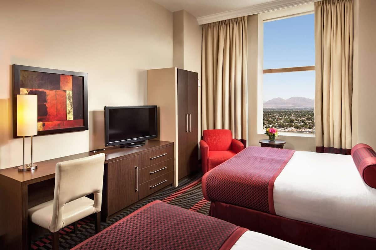 Habitación de hotel con cama, escritorio con televisor, silla, armario y vista a la ciudad.