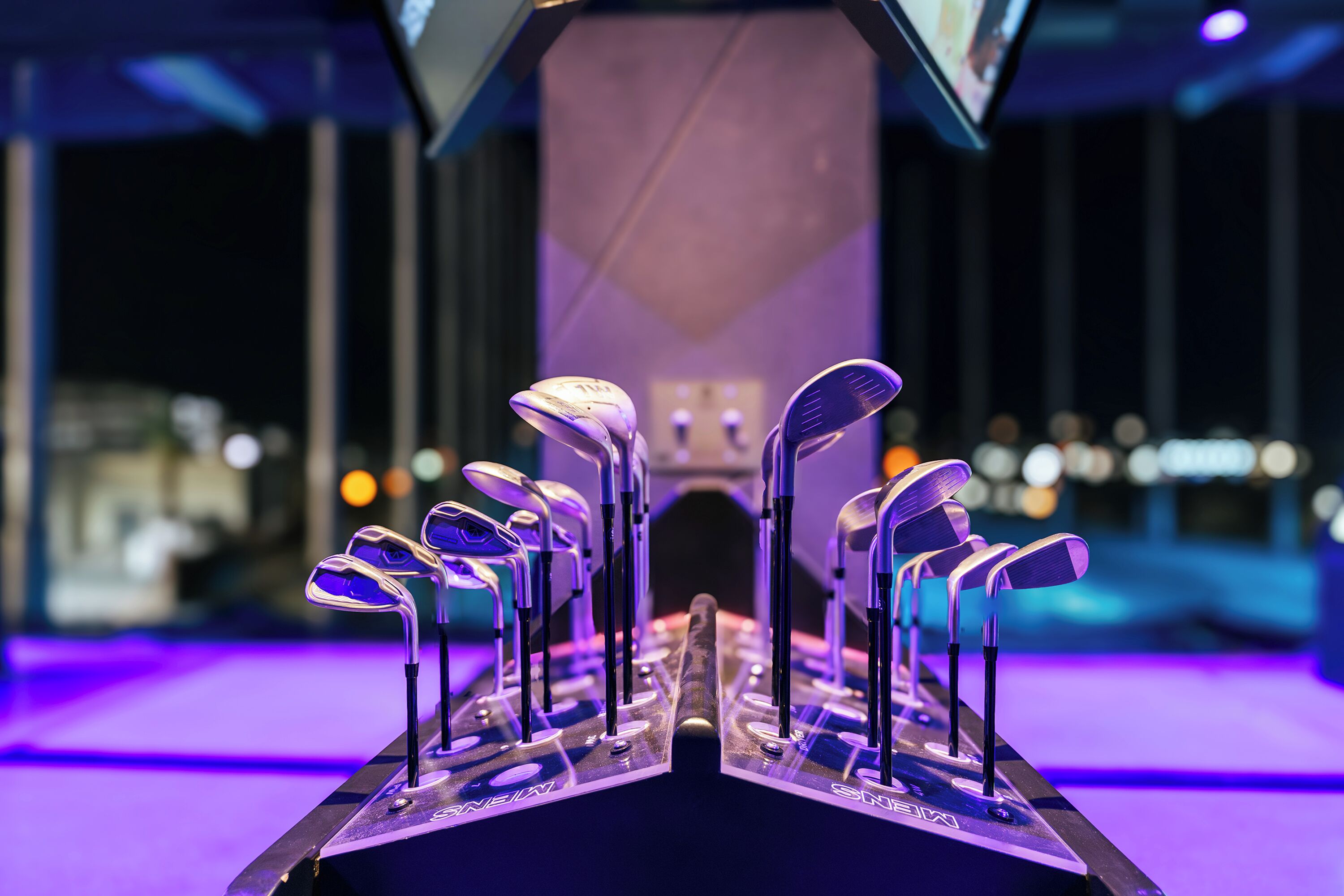 Una exhibición de palos de golf sobre un soporte con un fondo iluminado en morado.