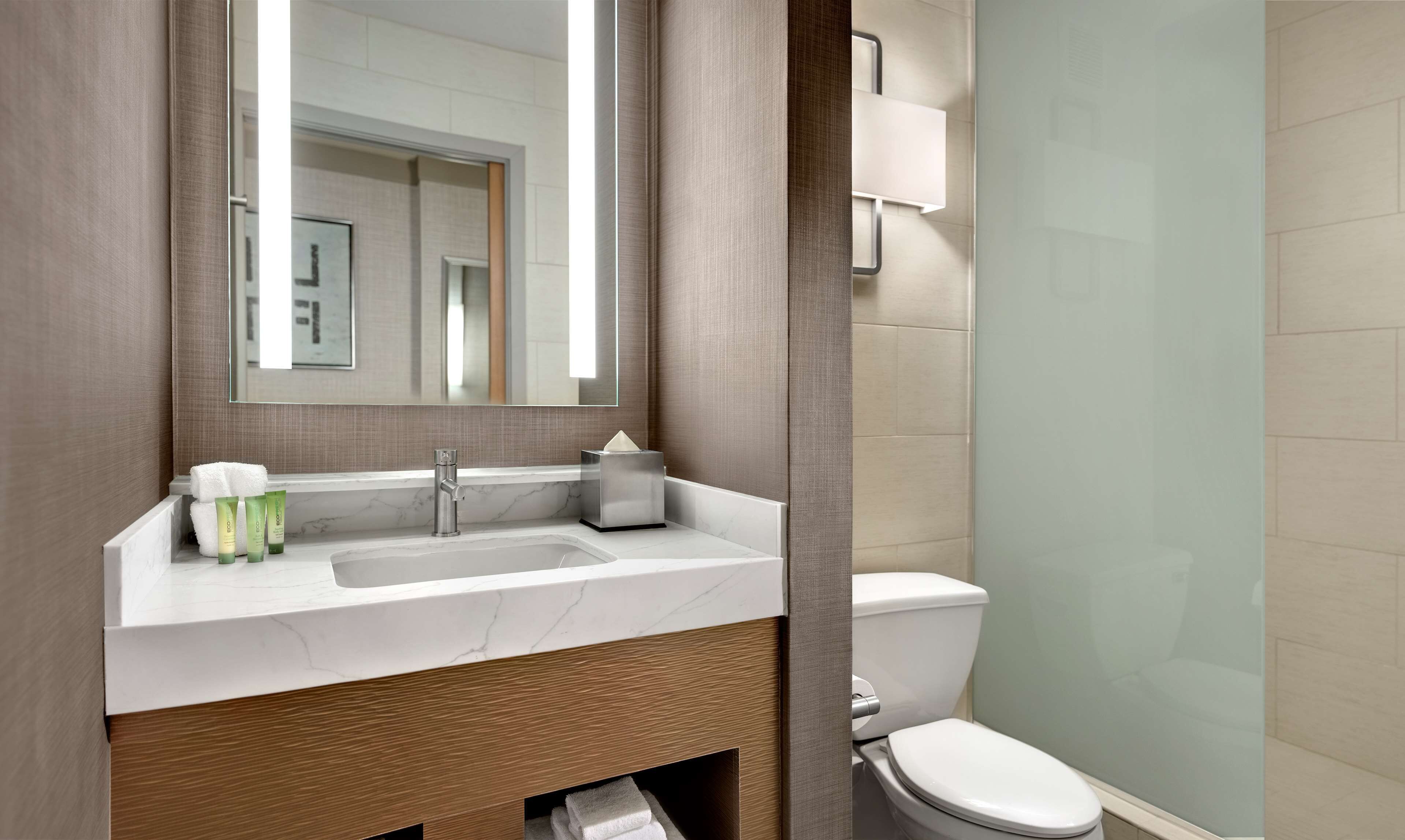 A modern bathroom with a marble sink, a mirror, a towel, and a toilet.