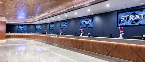 A modern reception area with a wooden ceiling, a long reception desk, and multiple monitors displaying the word "STRAT".