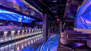Un espace bar moderne doté d’un long comptoir, de tabourets de bar et d’un coin salon avec des canapés et des tables.