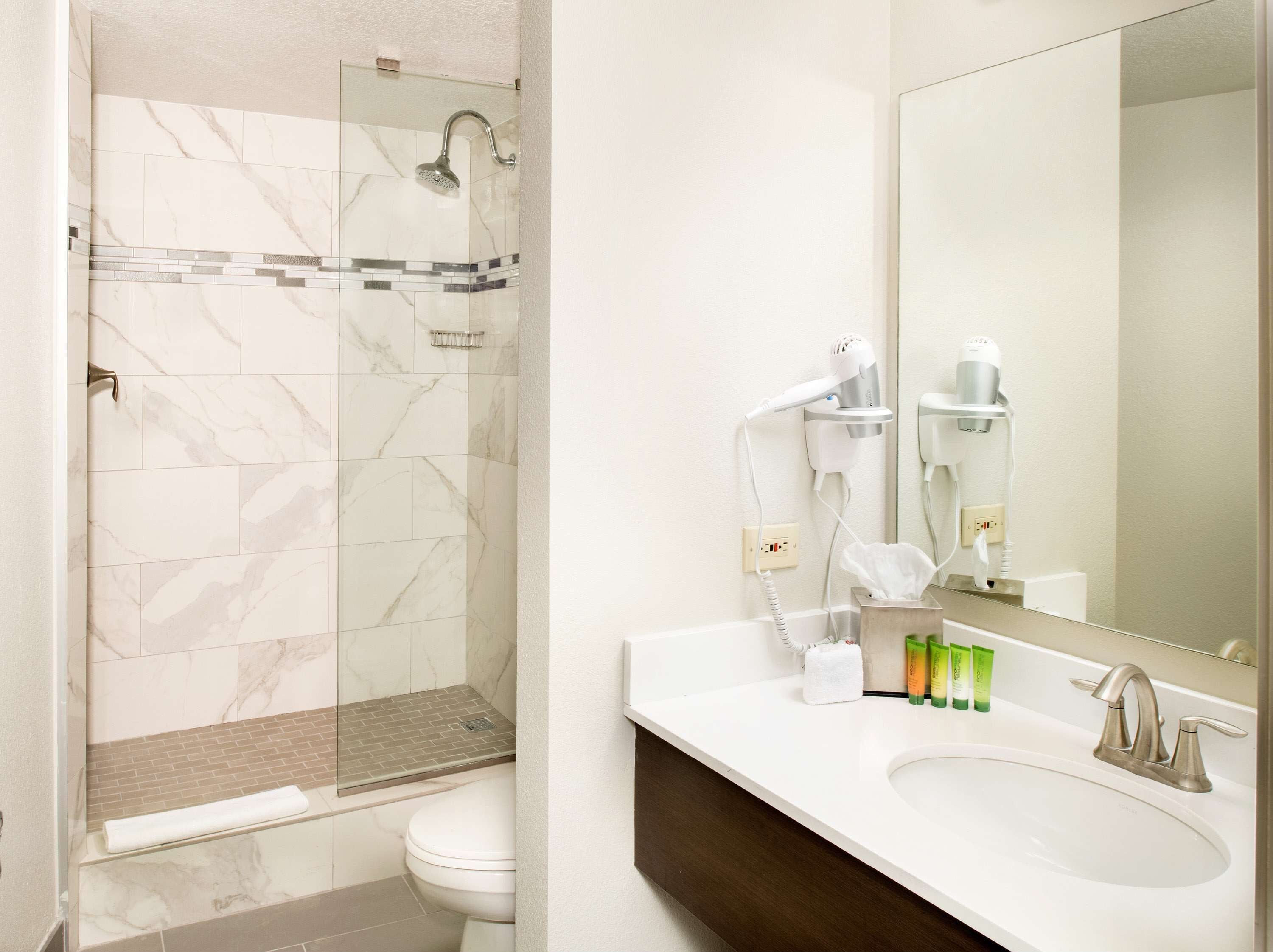 Une salle de bain avec une douche à parois de verre, des toilettes blanches, un lavabo avec un miroir et des articles de toilette posés sur le comptoir.
