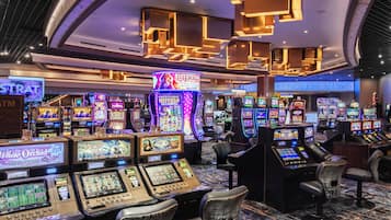 Un casino amb múltiples màquines escurabutxaques, tamborets de bar i un sostre amb aplics d'il·luminació geomètrica.