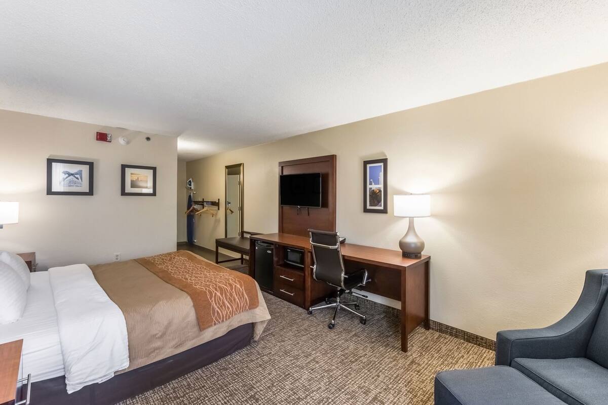 A hotel room with a bed, desk, chair, TV, and a lamp.
