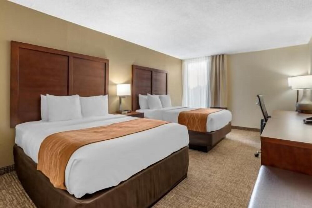 Une chambre d’hôtel avec deux lits, un bureau et une lampe.