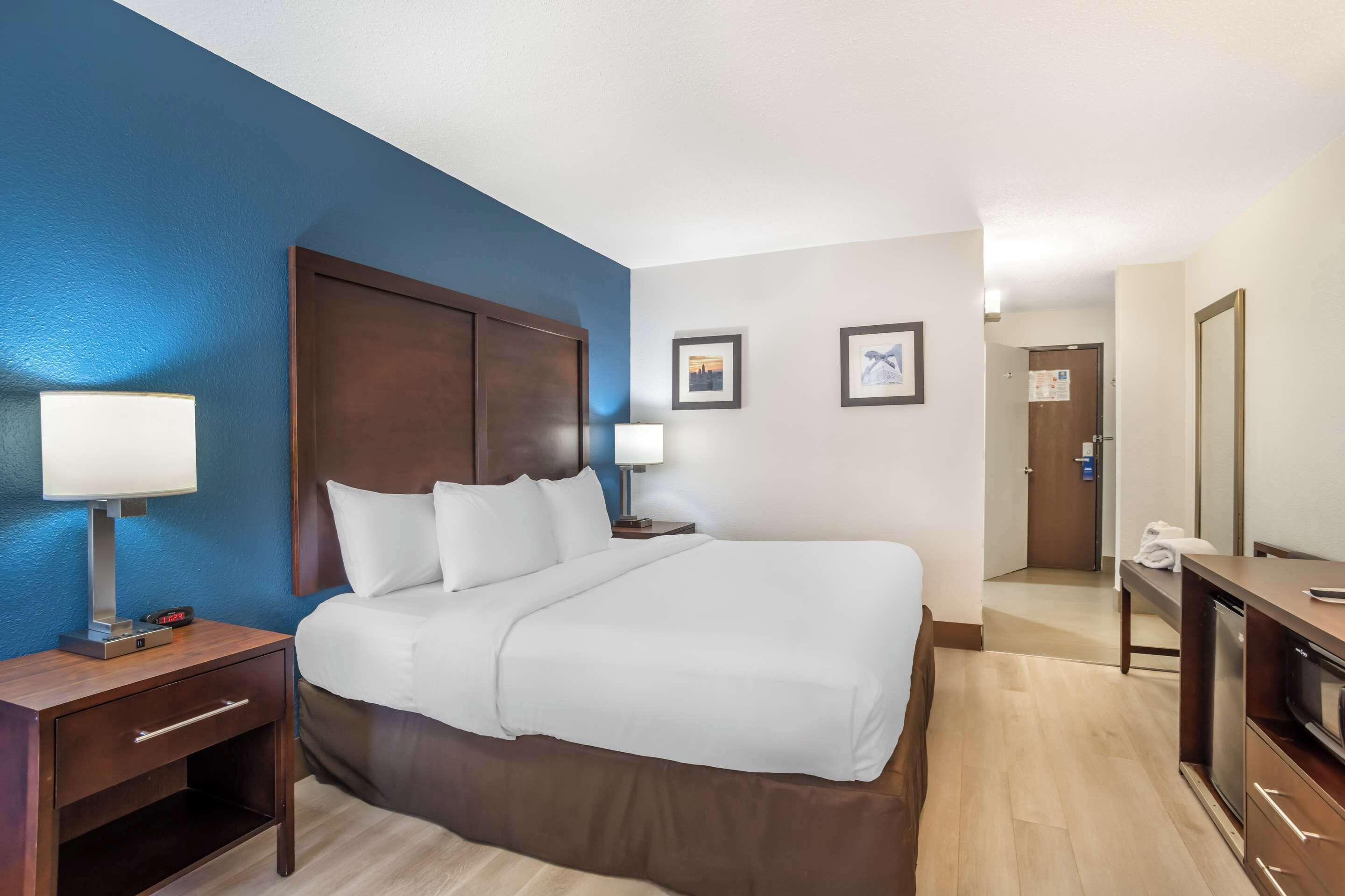 A hotel room with a large bed, two bedside tables with lamps, a wooden headboard, and a small desk with a television.