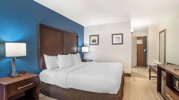 A hotel room with a large bed, two bedside tables with lamps, a wooden headboard, and a small desk with a television.