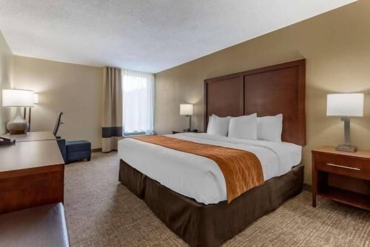 A hotel room with a large bed, two bedside tables with lamps, a desk, and a chair.